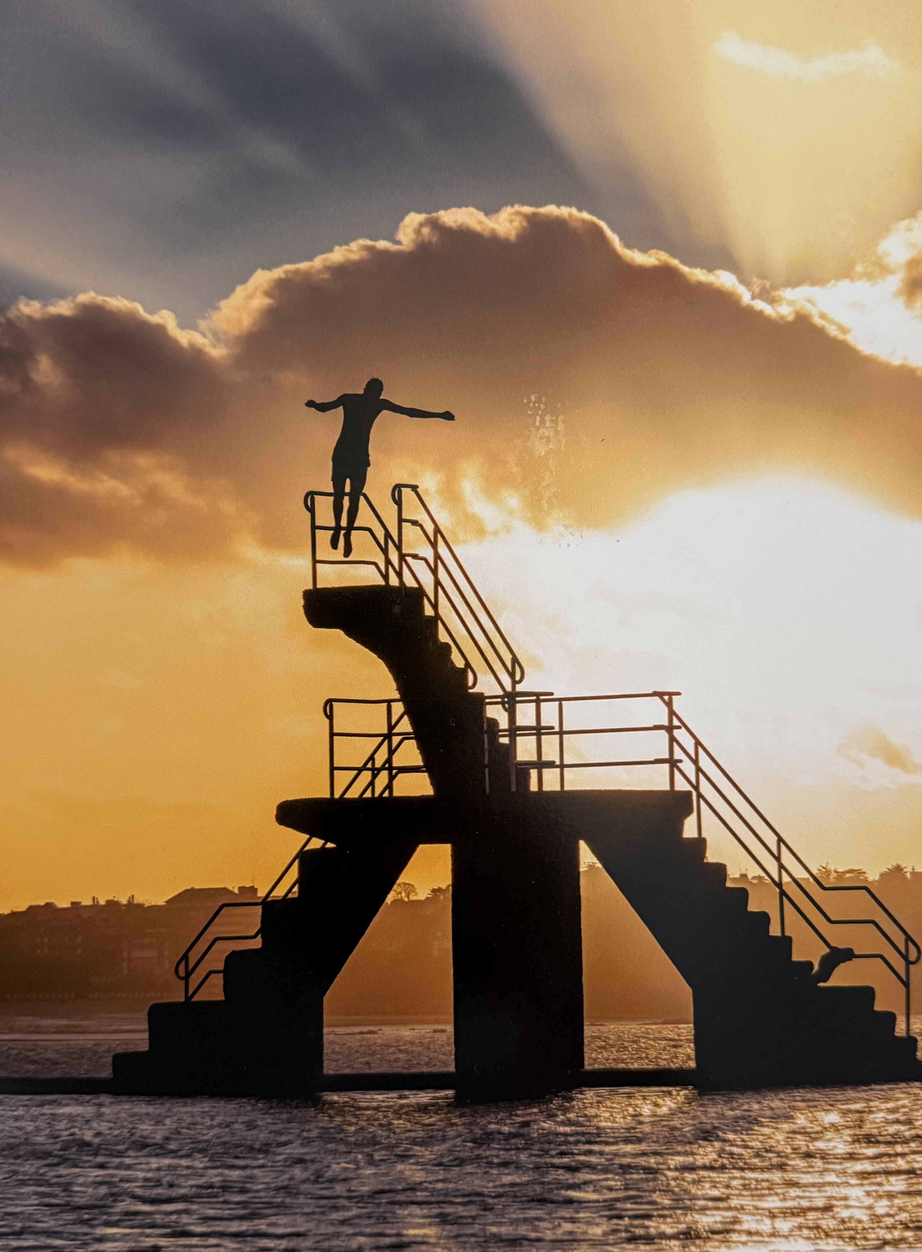 Silhouette au sommet d'un plongeoir au coucher de soleil, symbolisant le lâcher-prise et la transformation